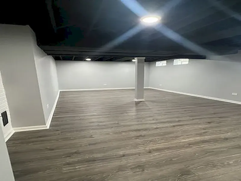 Empty basement room with gray walls, dark wood floors, and bright overhead light.