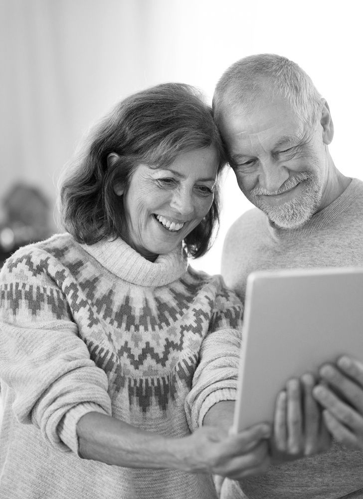 Smiling couple looking at a tablet together indoors, wearing cozy sweaters