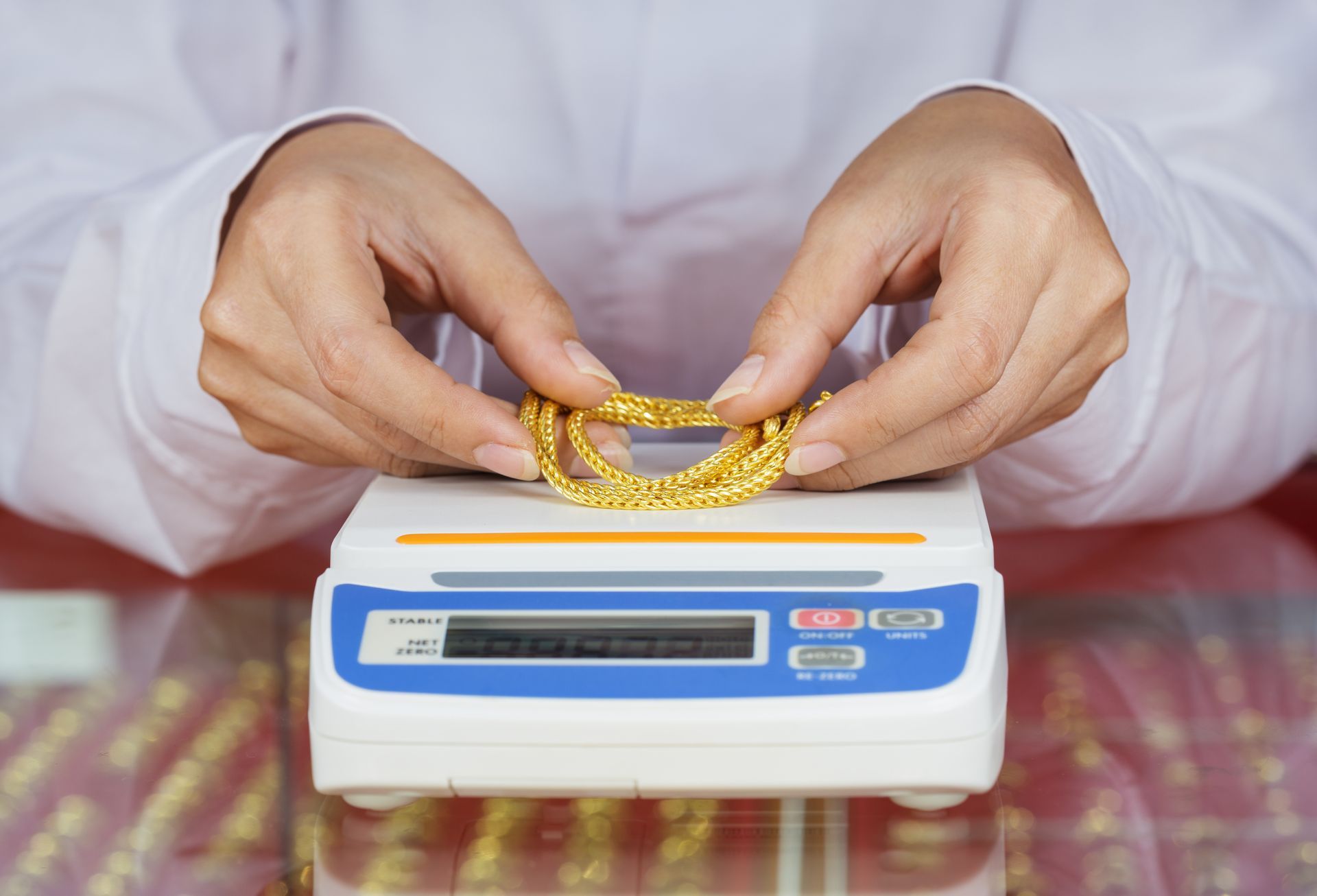 Hands weighing a gold necklace on a digital jewelry scale