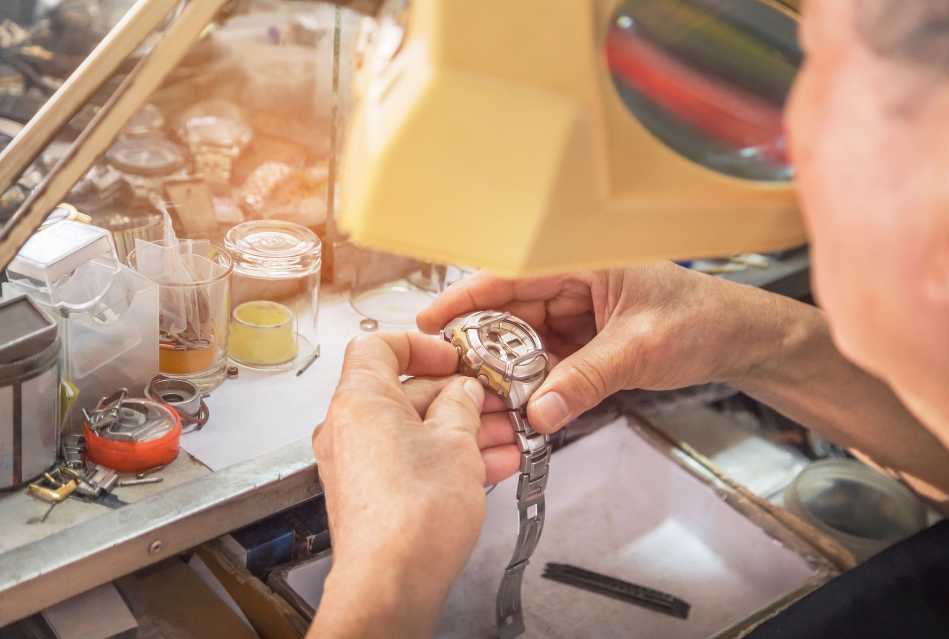 Watchmaker repairing a wristwatch at a workbench with tools and parts nearby