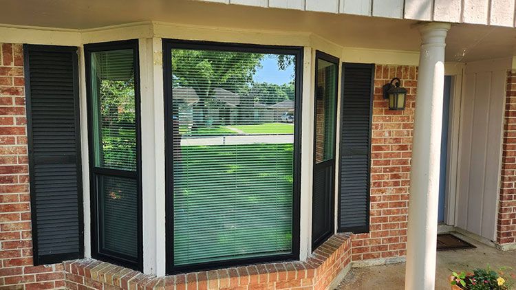 Bay window with black trim, black shutters, and brick facade.