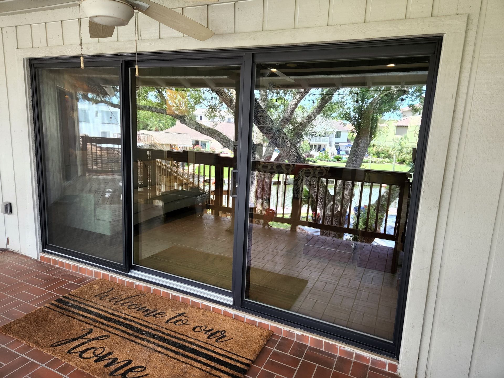 Sliding glass door opens to a deck with railing, trees visible through the windows, welcome mat.