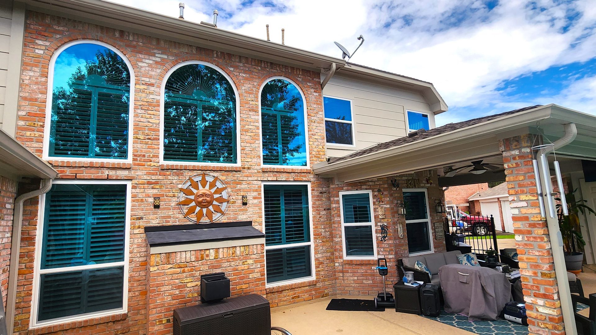 Brick house exterior with blue-tinted windows reflecting trees and sky; a covered patio on the right.