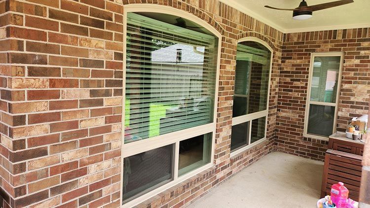 Brick wall with arched window, blinds, and a patio area with a ceiling fan.