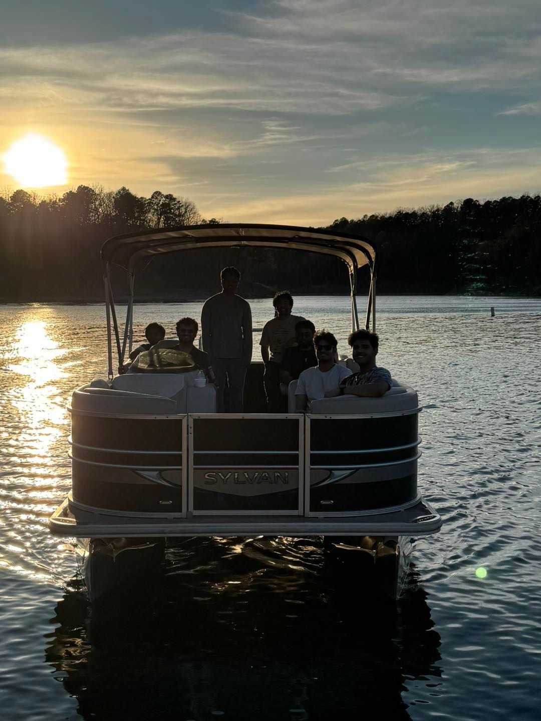 A group of people sitting on a pontoon boat on a lake at sunset.