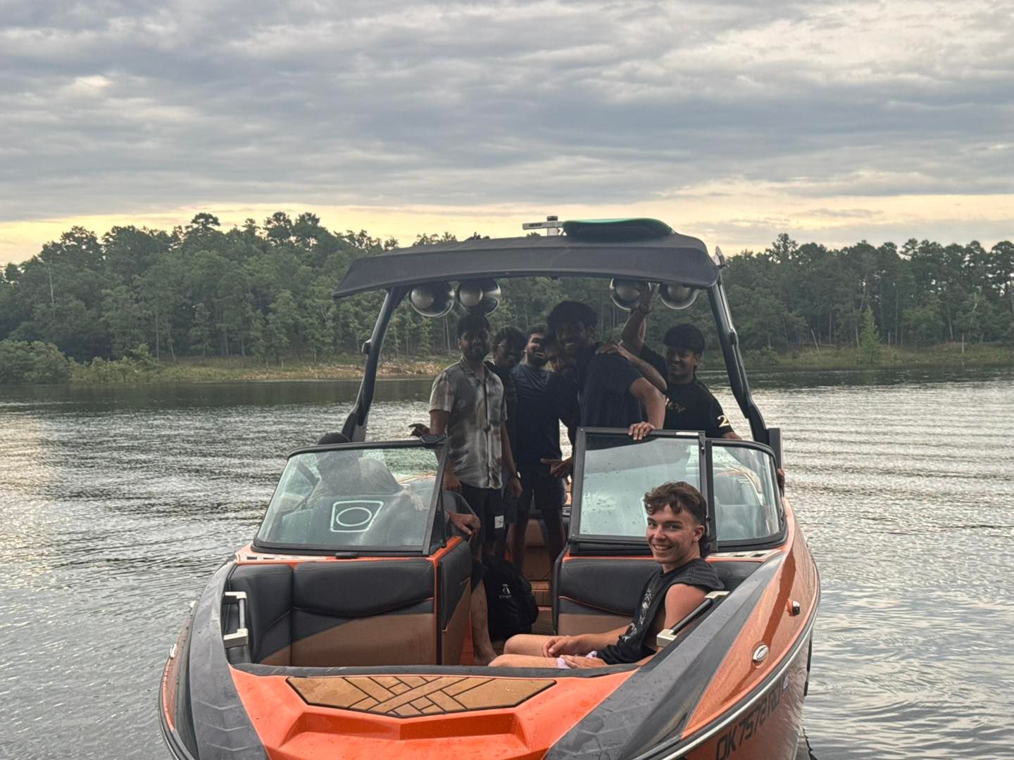 A group of people relaxing on an orange and black boat on a lake under a cloudy sky.