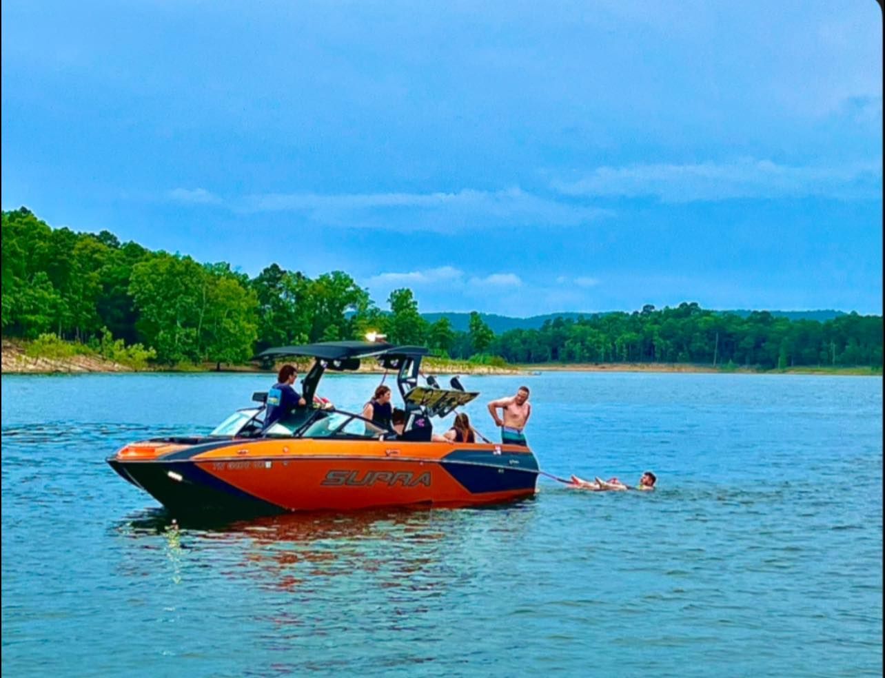 An orange and black motorboat on a lake with several people on board and one person swimming behind it.