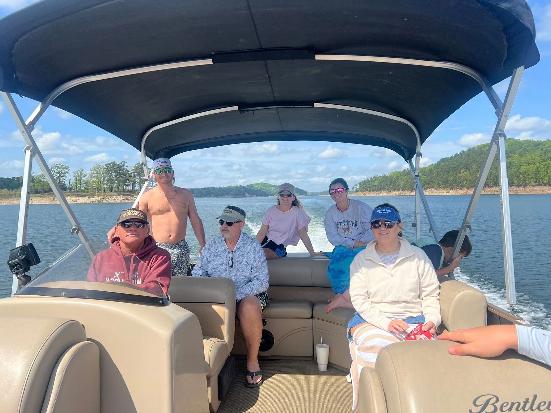 A group of people sitting on a pontoon boat on a lake under a clear blue sky.