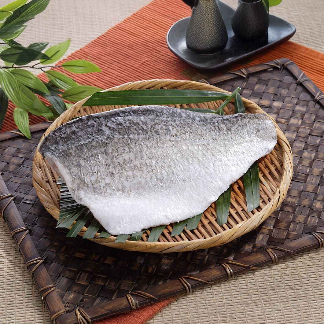 魚片放在編織籃中,籃裡放著綠葉,籃子下面是花紋墊子,背景是深色陶器。