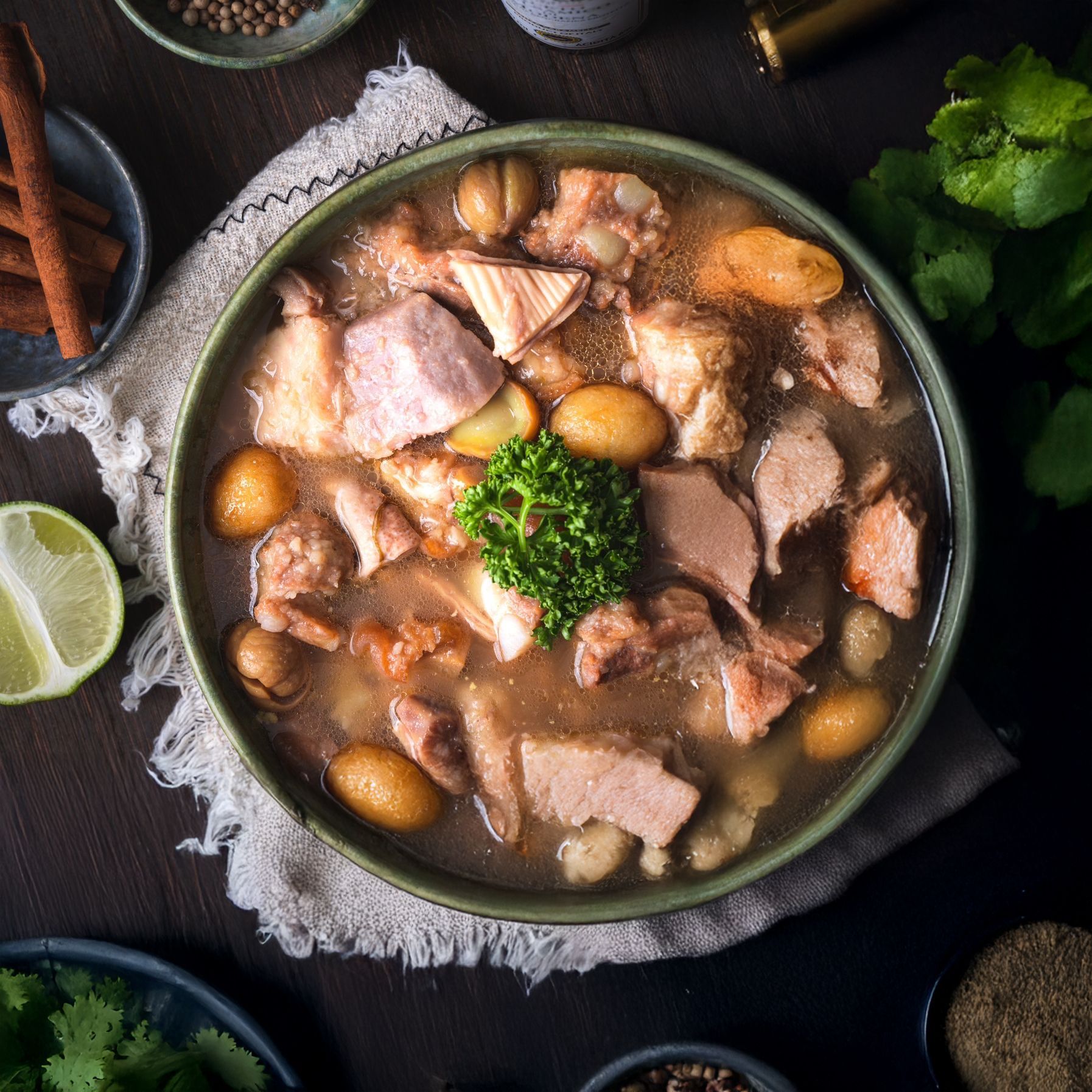 盛在綠色碗裡的肉湯,裡面有肉和土豆,周圍點綴著青檸、香菜和香料等配料。