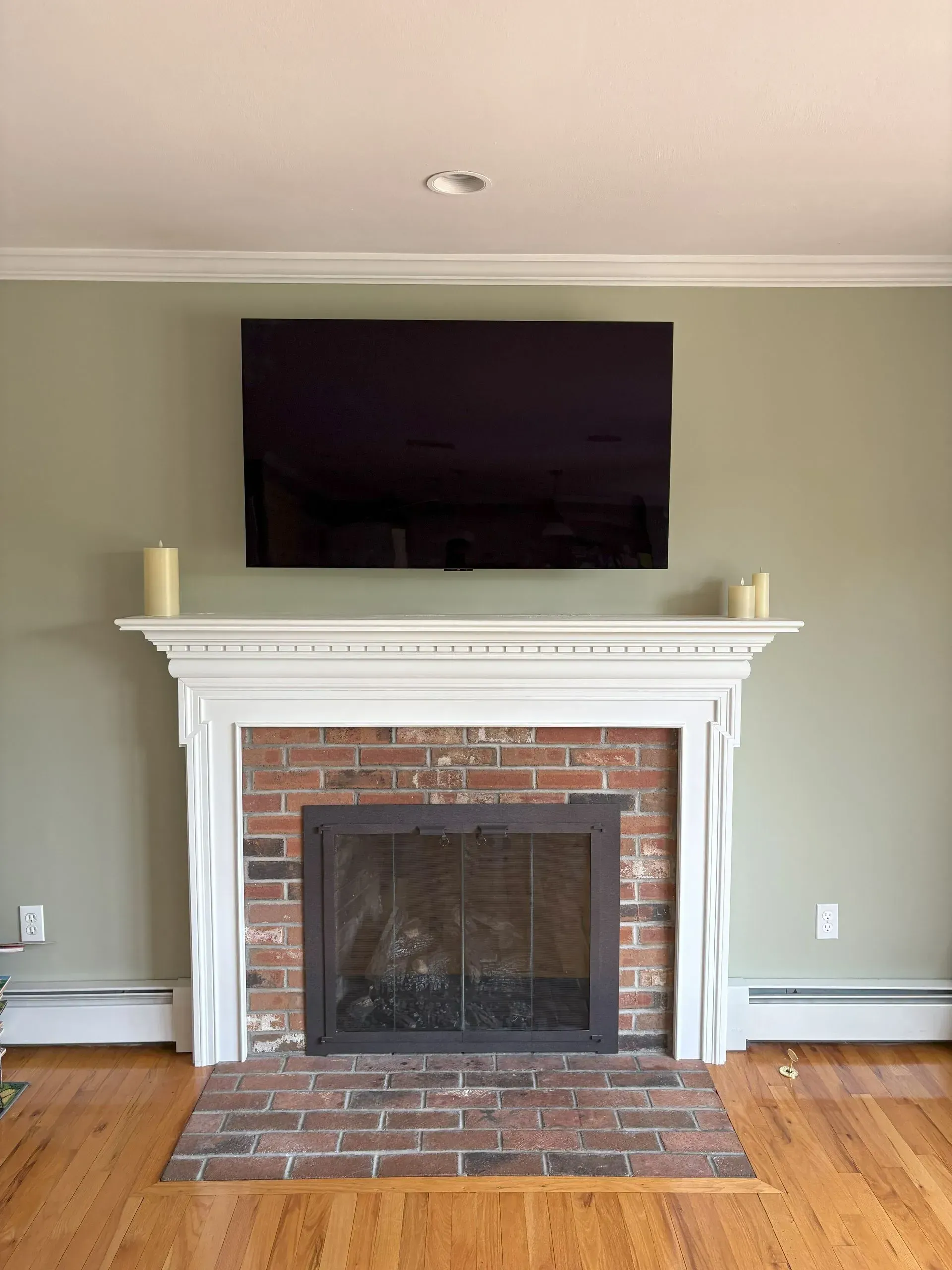 Living room fireplace with a mounted flat-screen TV, white mantel, brick surround, and hardwood floors