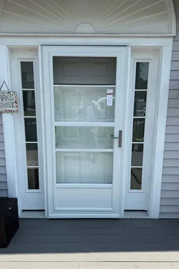 Front entry with white storm door, sidelights, and gray siding on a porch.