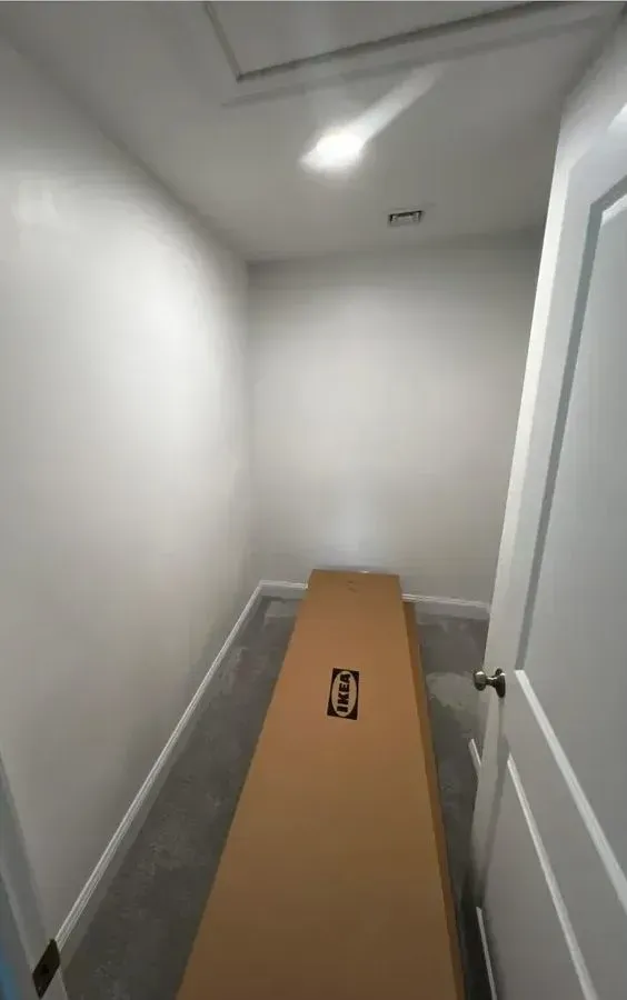 Narrow white hallway with a long cardboard box lying on the floor near a doorway.