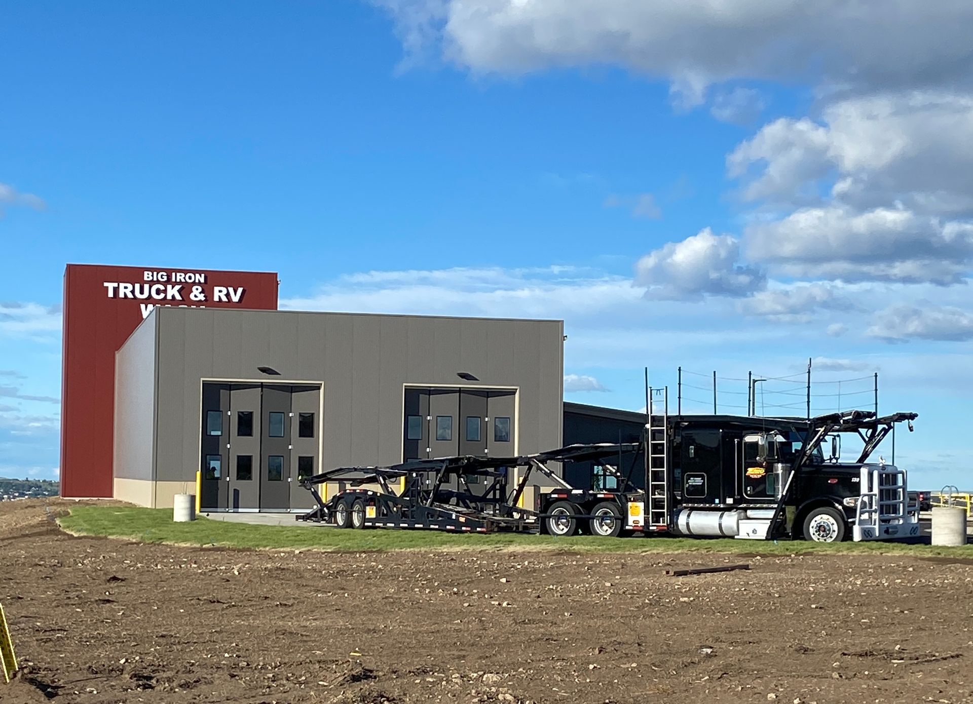 Semi-truck and trailer parked beside a truck and RV building under a blue sky