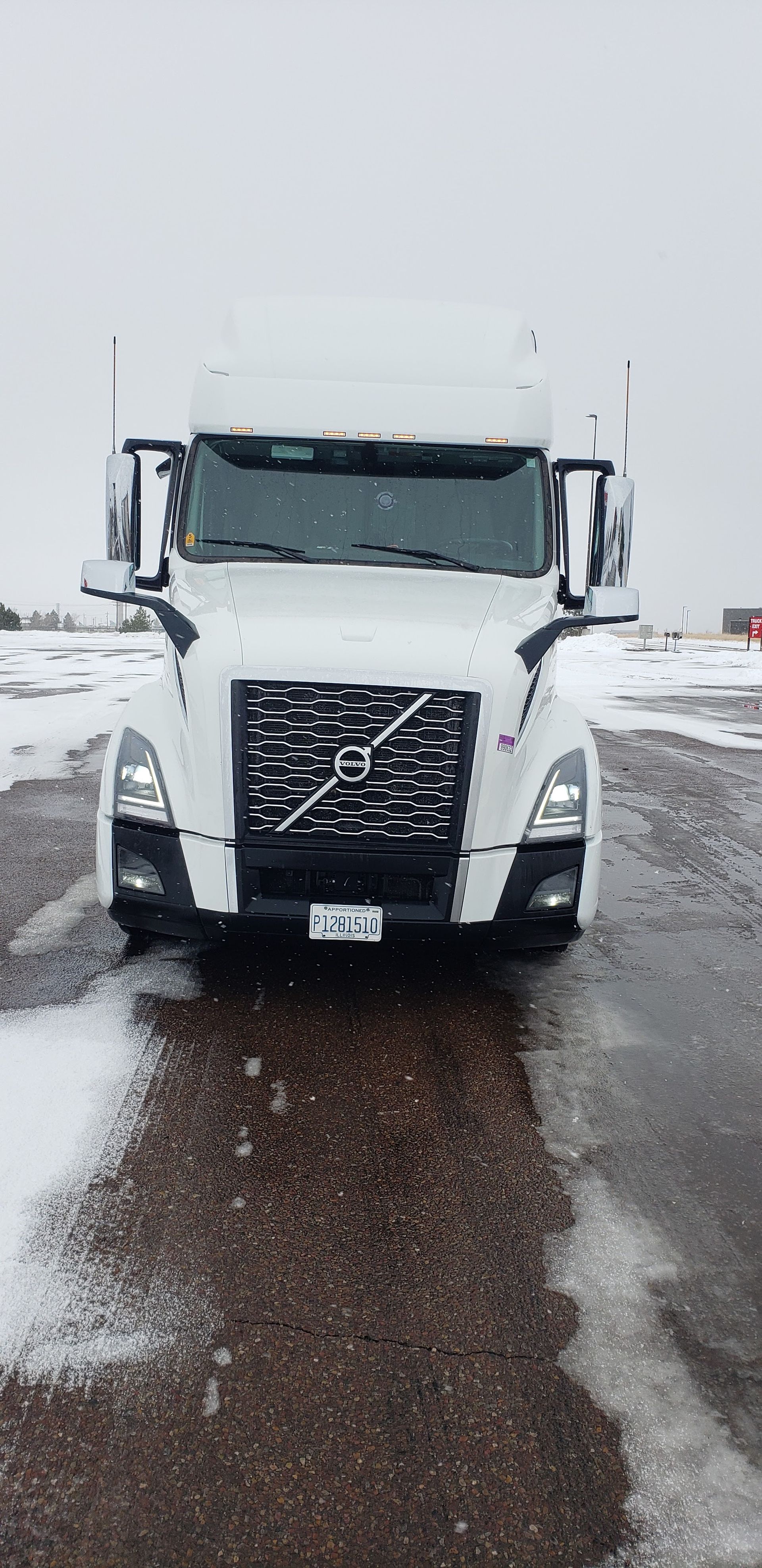 White semi-truck driving on a wet, snowy road in a wintry scene