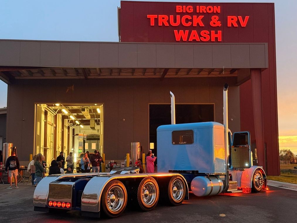 Custom white semi truck parked outside Big Iron Truck & RV Wash at night, garage lights glowing