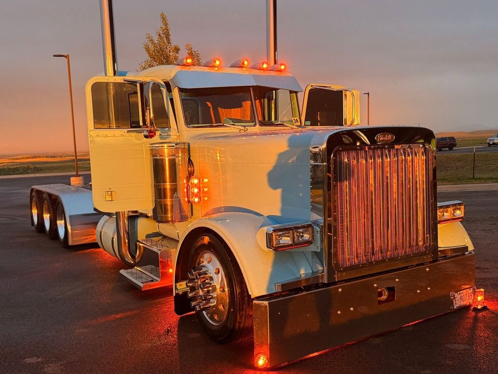 Classic white semi truck with chrome grille parked at sunset, amber lights glowing on a wet road.