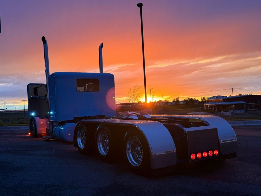 Blue semi truck at sunset with orange sky and red taillights on a roadway