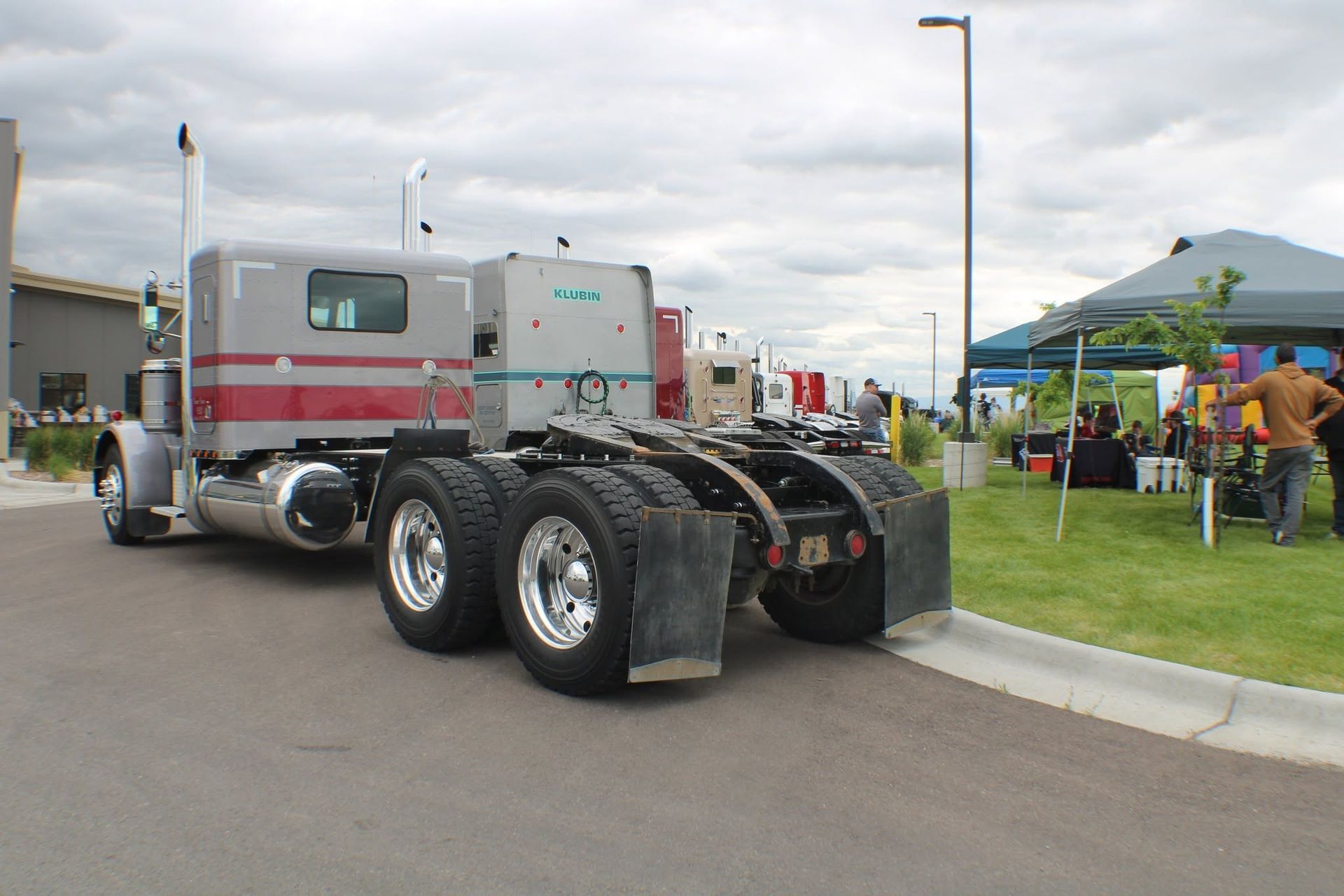 Semi-truck cab parked near a grassy event area with tents and people in the background