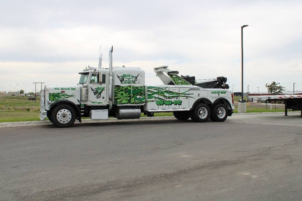 White and green tow truck parked on a roadside in an open lot