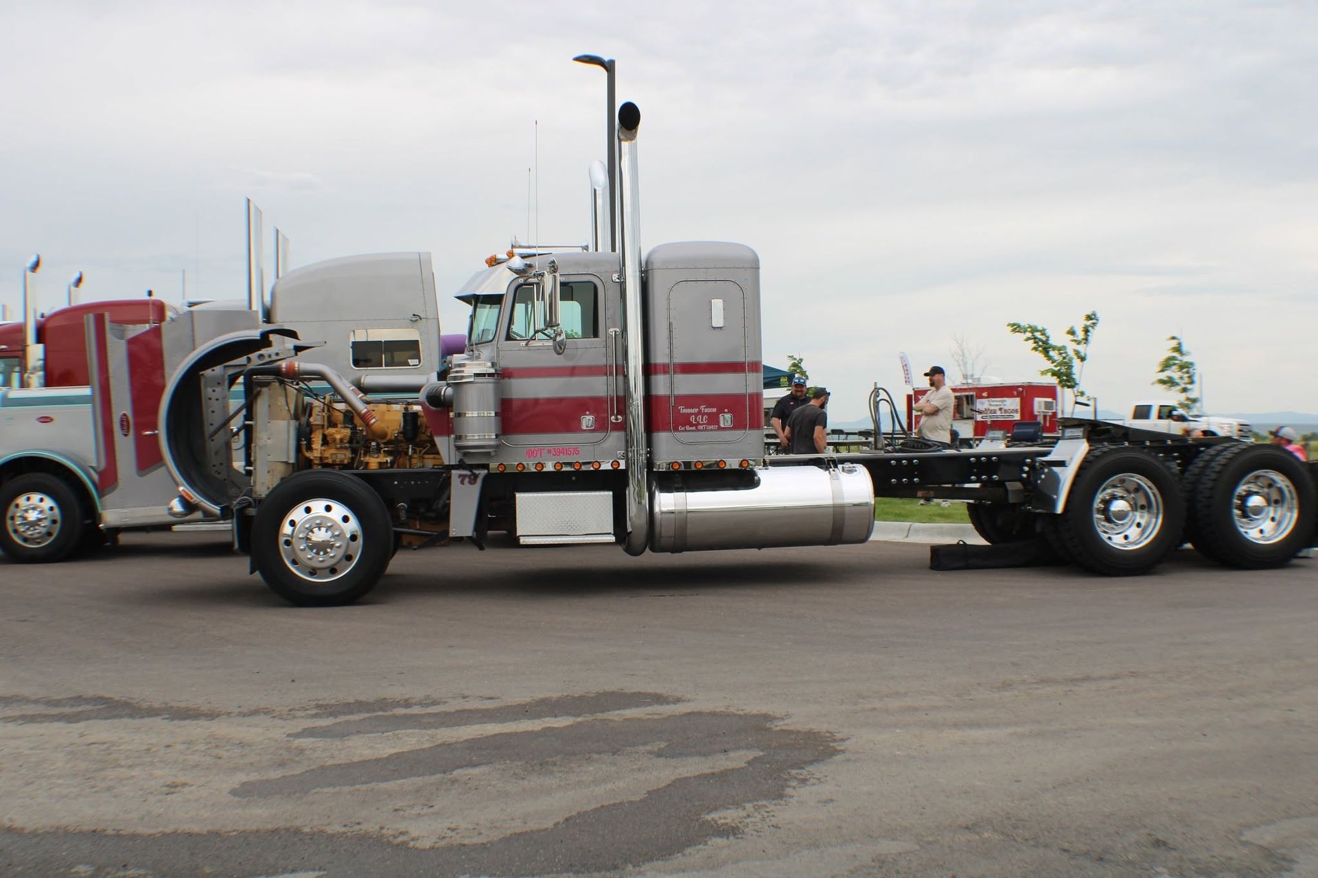 Red semi-truck cab with chrome fuel tank parked on pavement, side view under cloudy sky