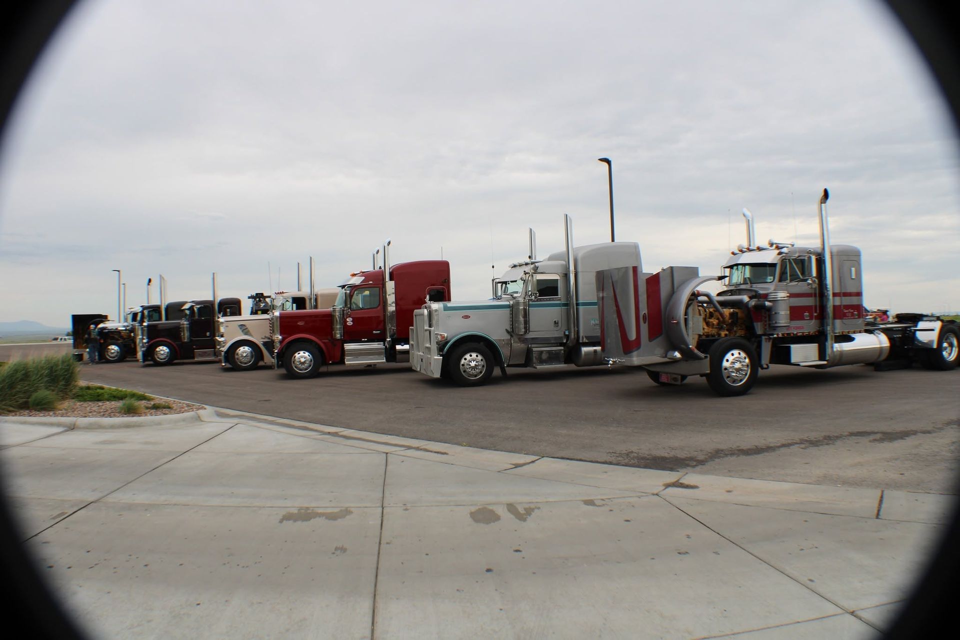 Line of semi trucks parked along a road in an open, cloudy landscape