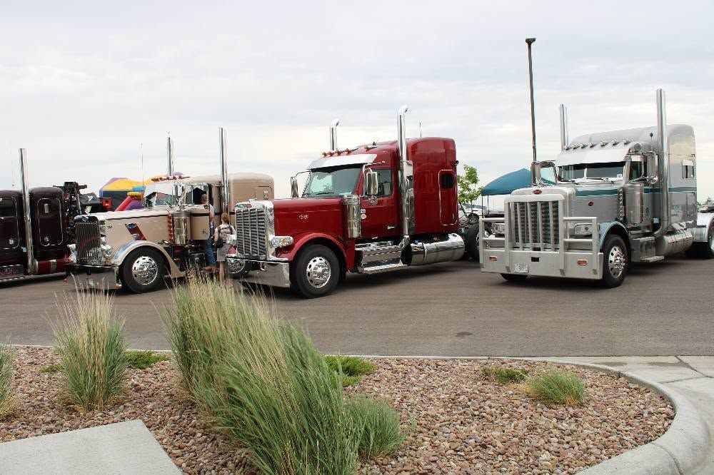 Several semi trucks parked on gravel near a road, including red and silver cabs.