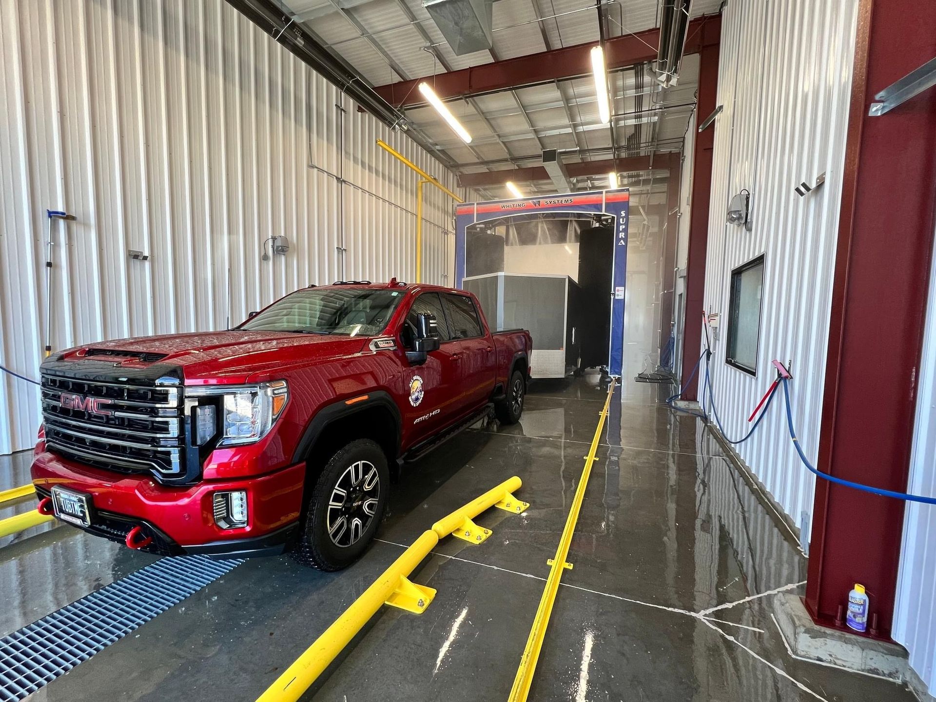 Red pickup truck in a narrow auto shop bay with yellow wheel guides and white walls