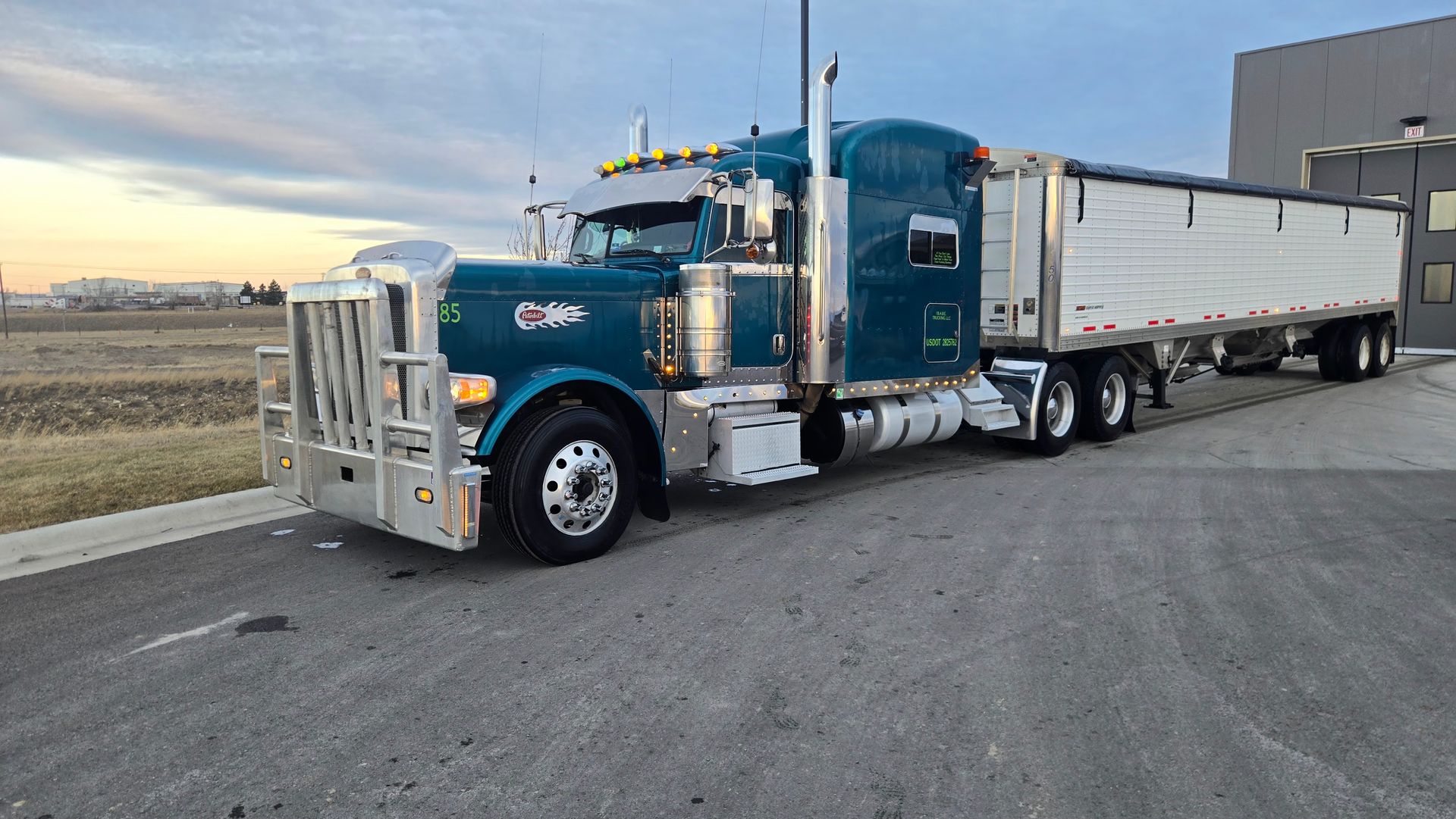 Blue semi-truck with white trailer parked on a roadside at dusk