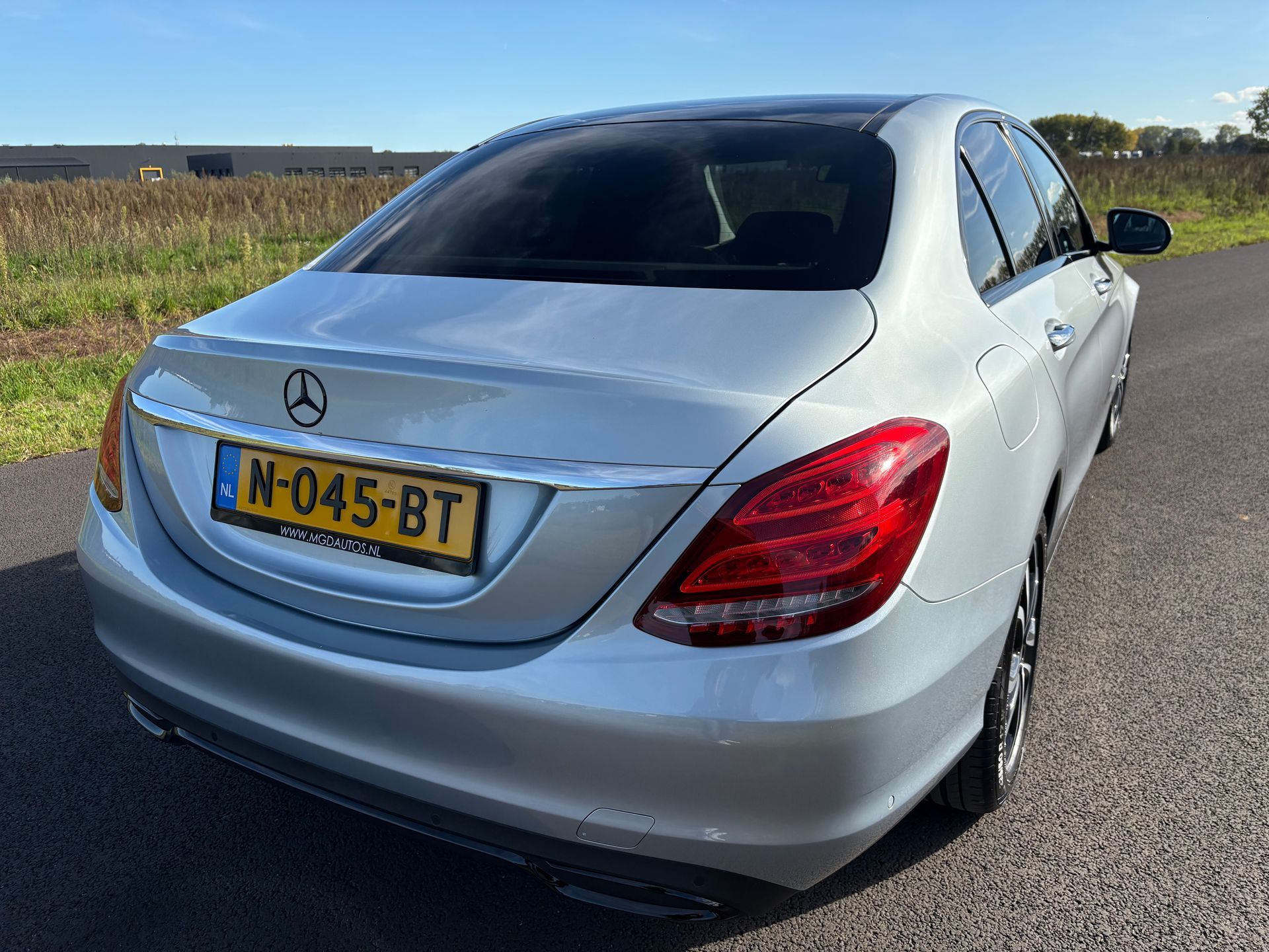 Zilverkleurige Mercedes sedan geparkeerd op een landweg, achterkant gezien met Nederlands kenteken.