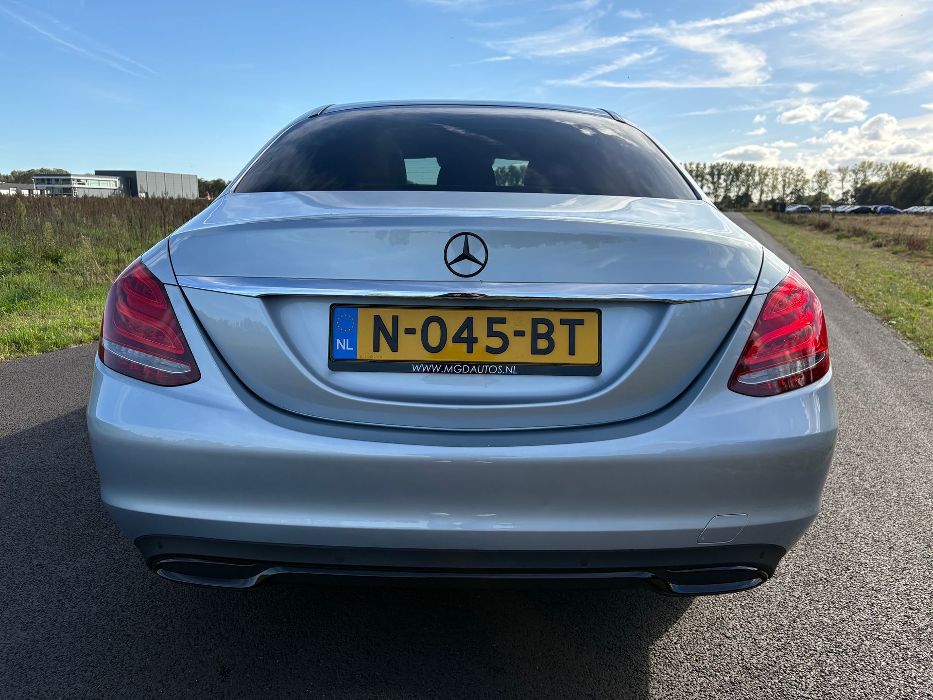 Achteraanzicht van een zilverkleurige Mercedes sedan met een Nederlands kenteken op een landweg.