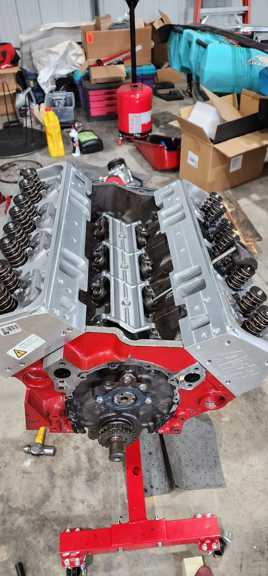 Disassembled engine parts laid out on a garage floor, with a red engine stand and tools nearby.