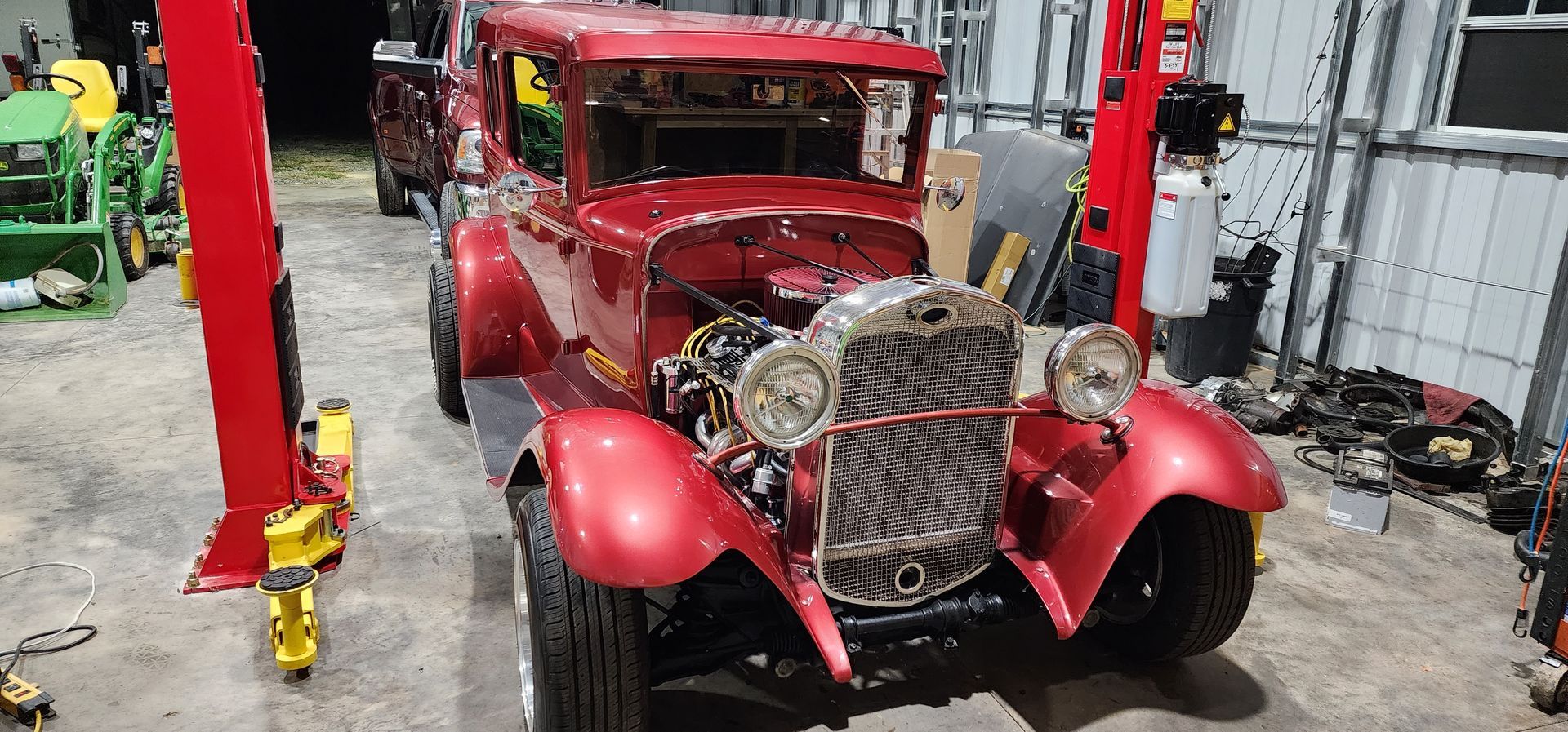 Red vintage car in a garage with exposed engine, framed by a red vehicle lift.