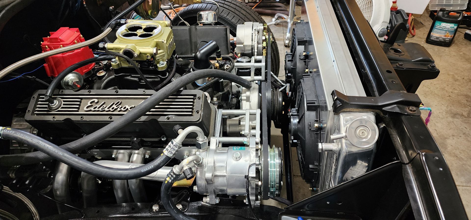 Close-up of a car engine bay with polished metal components, hoses, and a red battery on the left