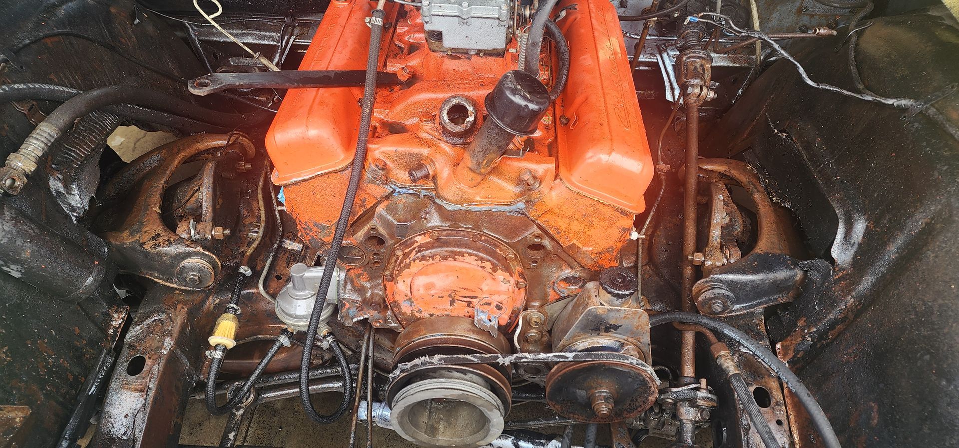 Orange engine block with hoses and metal parts, covered in grime and liquid in a workshop.