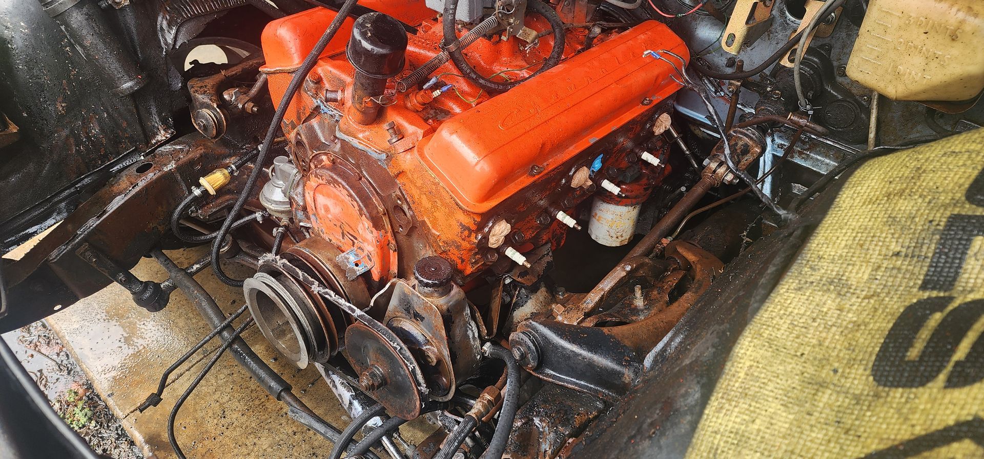 Charred orange engine in a burned vehicle wreck, with twisted wires and debris around it