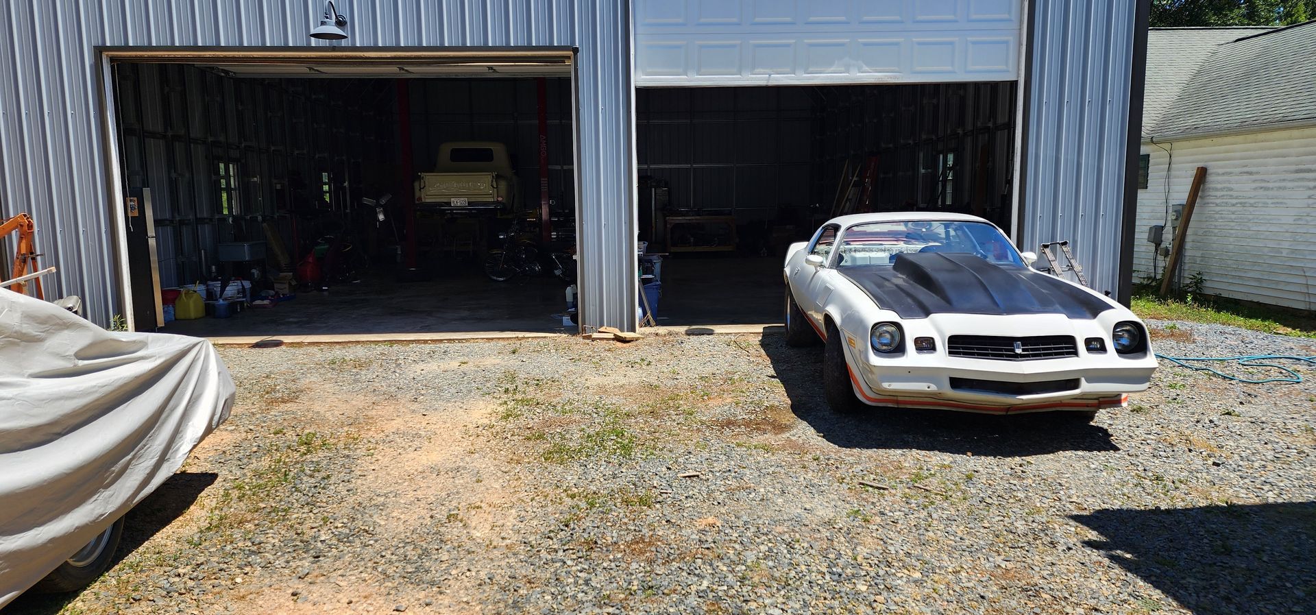 White sports car parked outside two open garages on a gravel driveway.