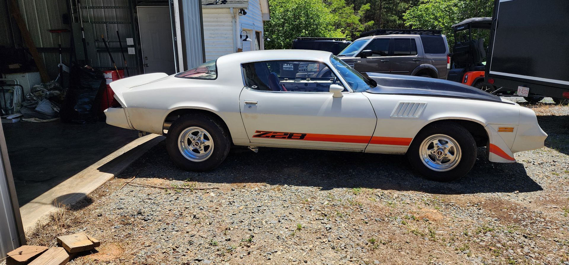 White classic muscle car with black hood stripes parked in a driveway under bright sun