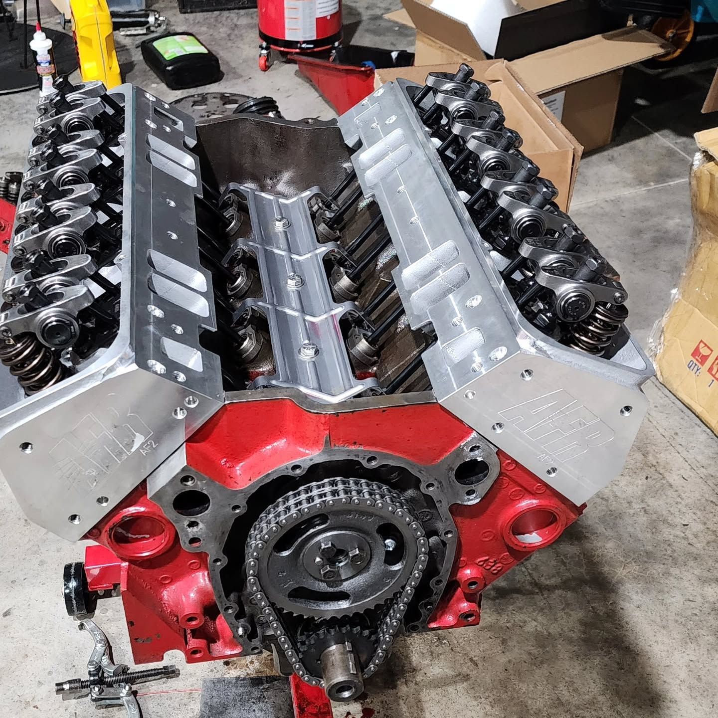Red V8 engine block with silver cylinder heads and black valve train in a workshop setting