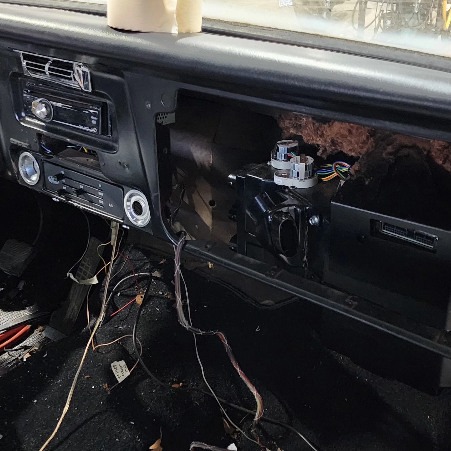 Car dashboard with glovebox removed, exposing wires and open passenger-side compartment.