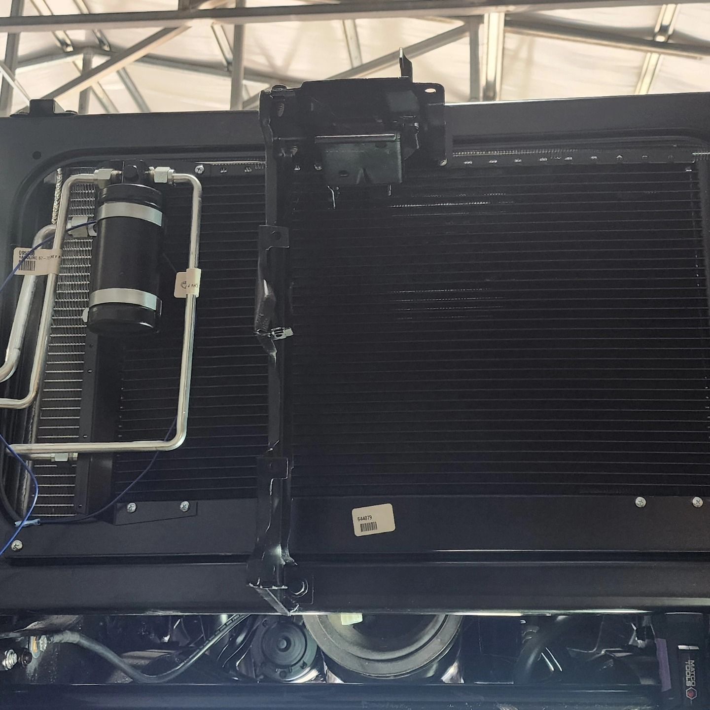 Black industrial machinery with large radiator-like panels and metal tubing inside a vehicle or equipment bay