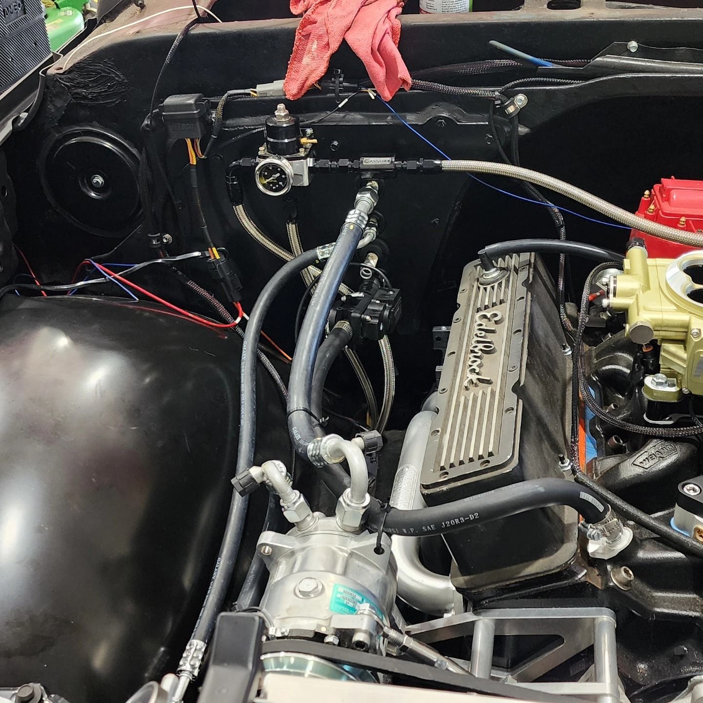 Car engine bay with exposed V8 engine, hoses, and wiring under the hood.