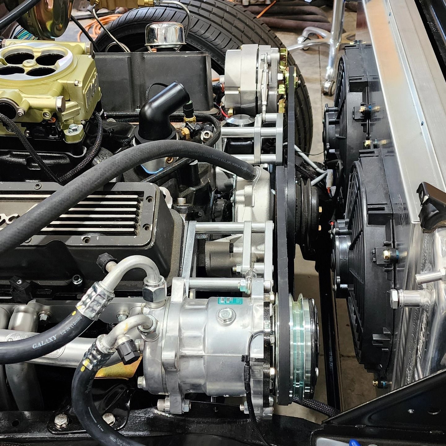 Close-up of a car engine bay with belts, hoses, and a silver compressor mounted near the radiator.