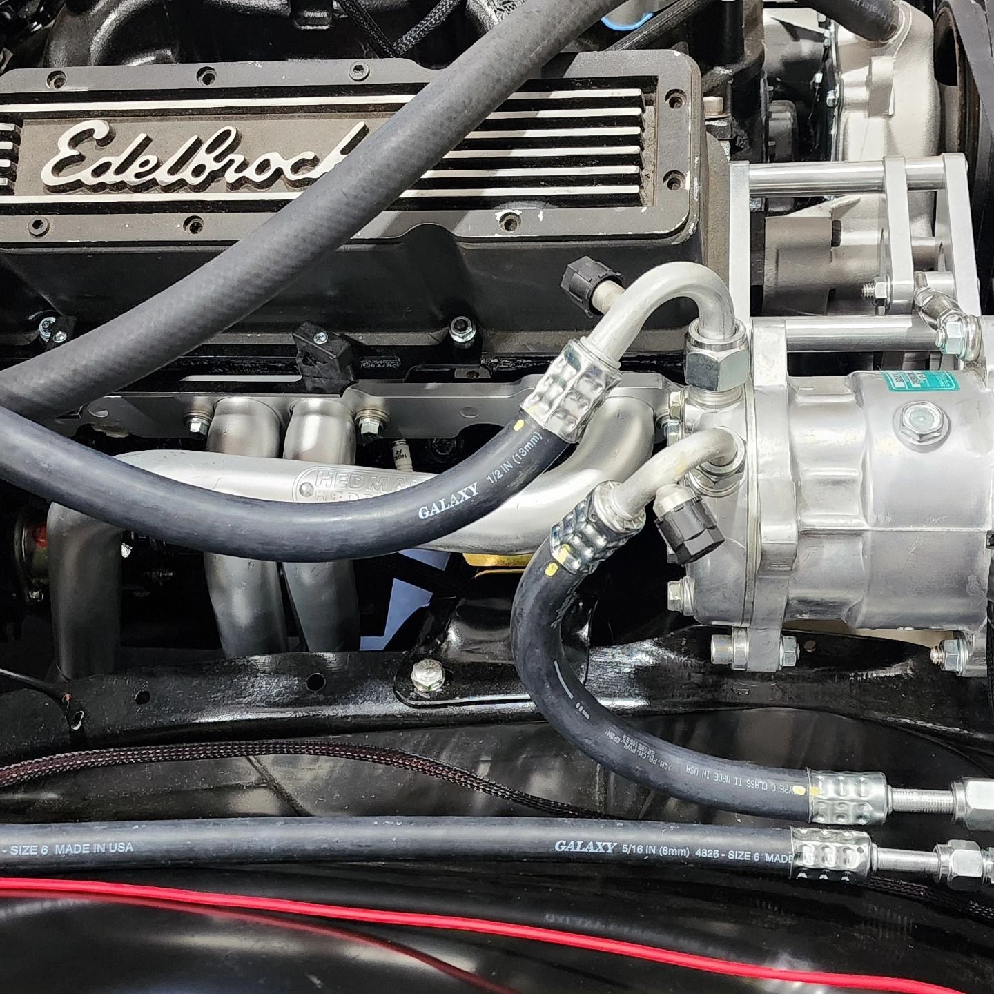 Close-up of an Edelbrock engine with black hoses and silver fittings in a car engine bay
