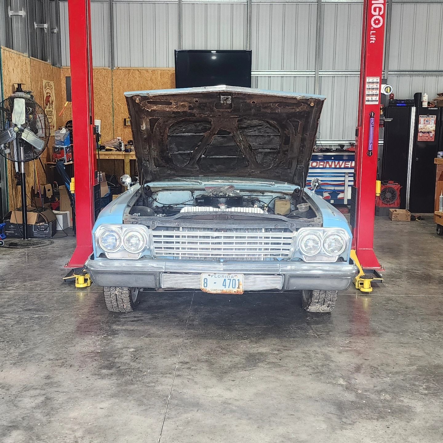 Classic silver car with hood open in an auto repair shop on lifts