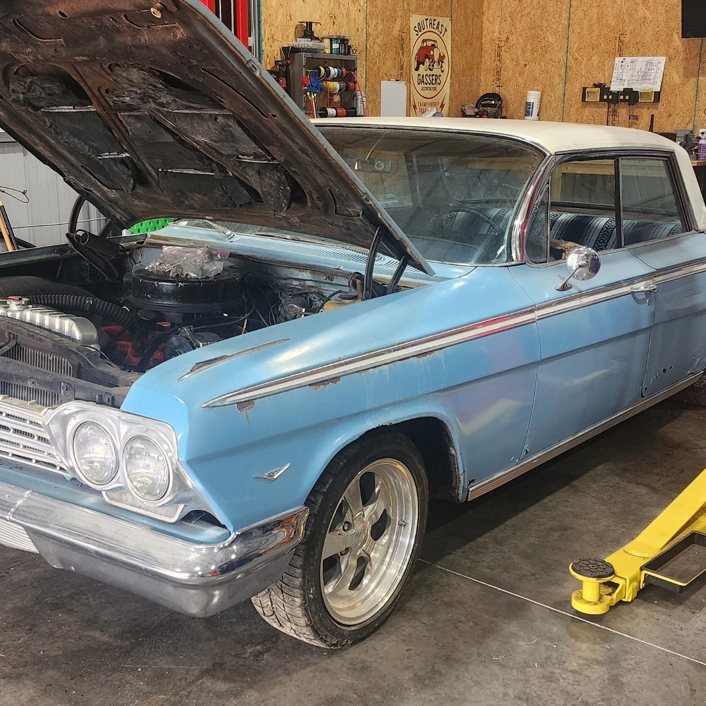 Light blue classic car in a garage with its hood open, showing chrome trim and front headlights