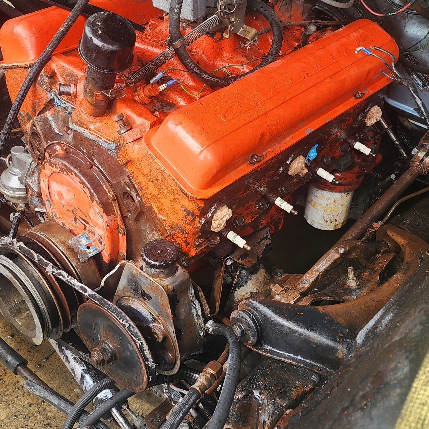 Orange engine block with exposed belts and hoses in a workshop setting
