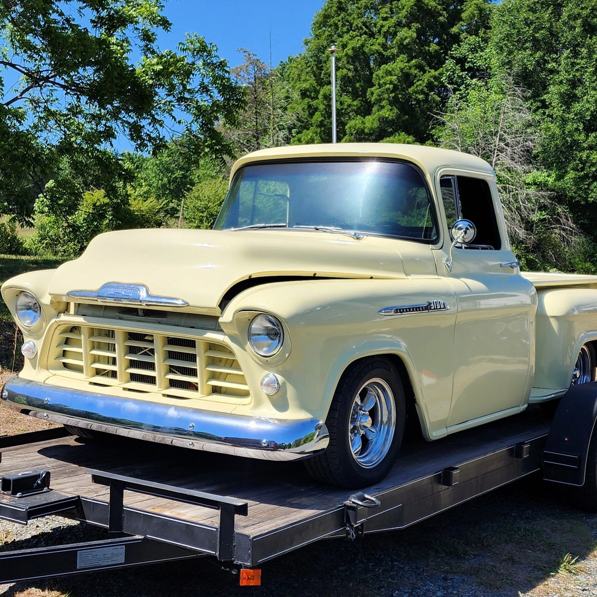 Cream vintage pickup truck on a trailer outdoors under bright sunlight