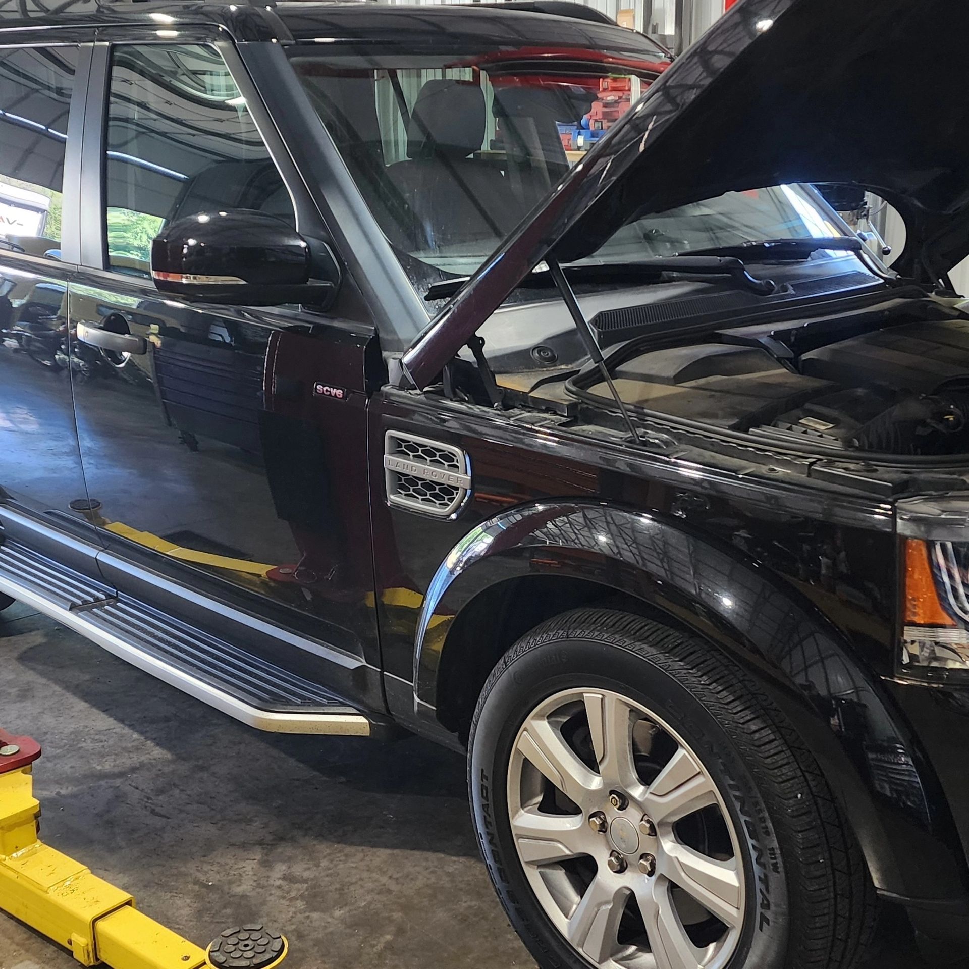 Black SUV with hood open in an auto shop, seen from the side on a lift bay
