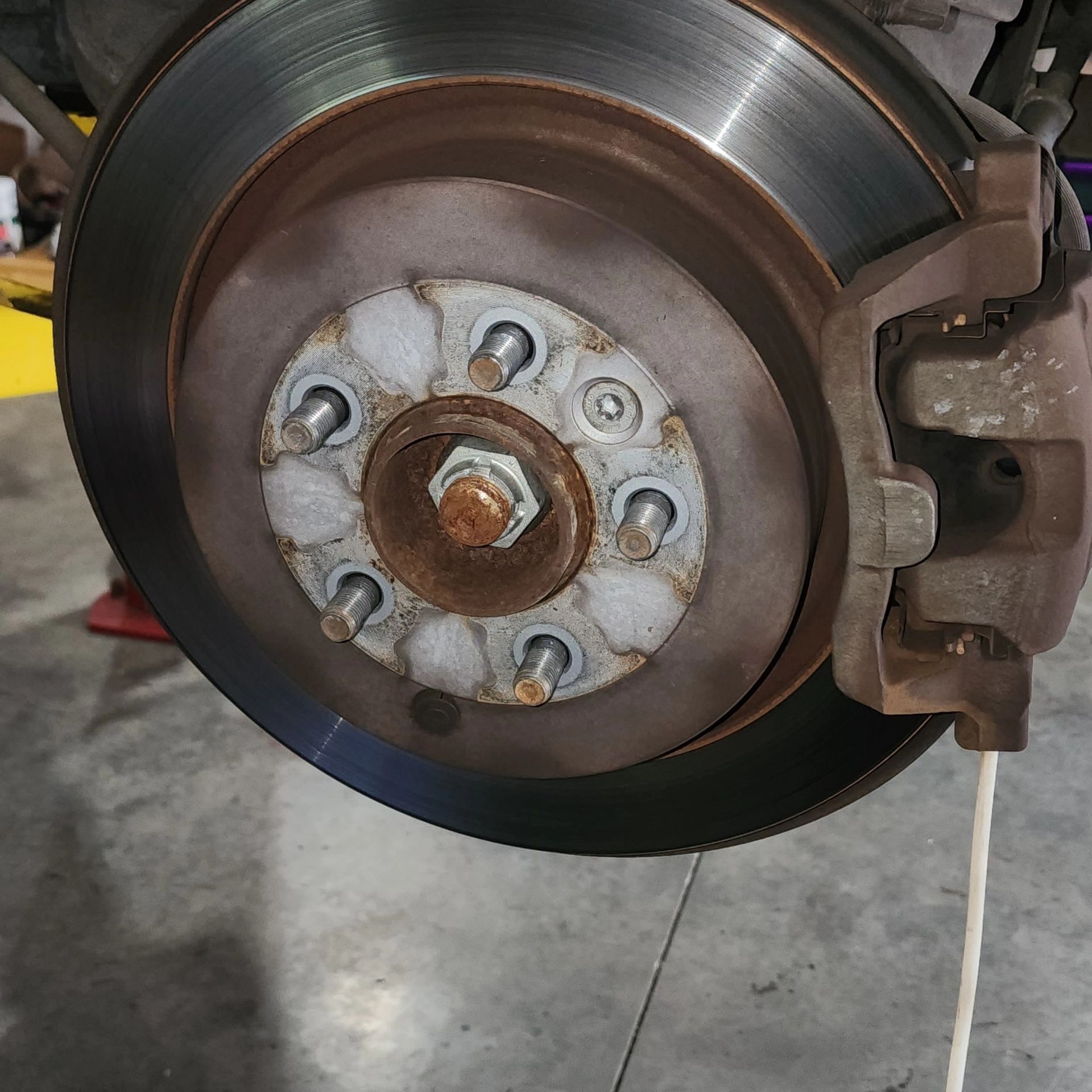 Close-up of a car brake disc and caliper with wheel removed, showing the rotor and lug nuts.